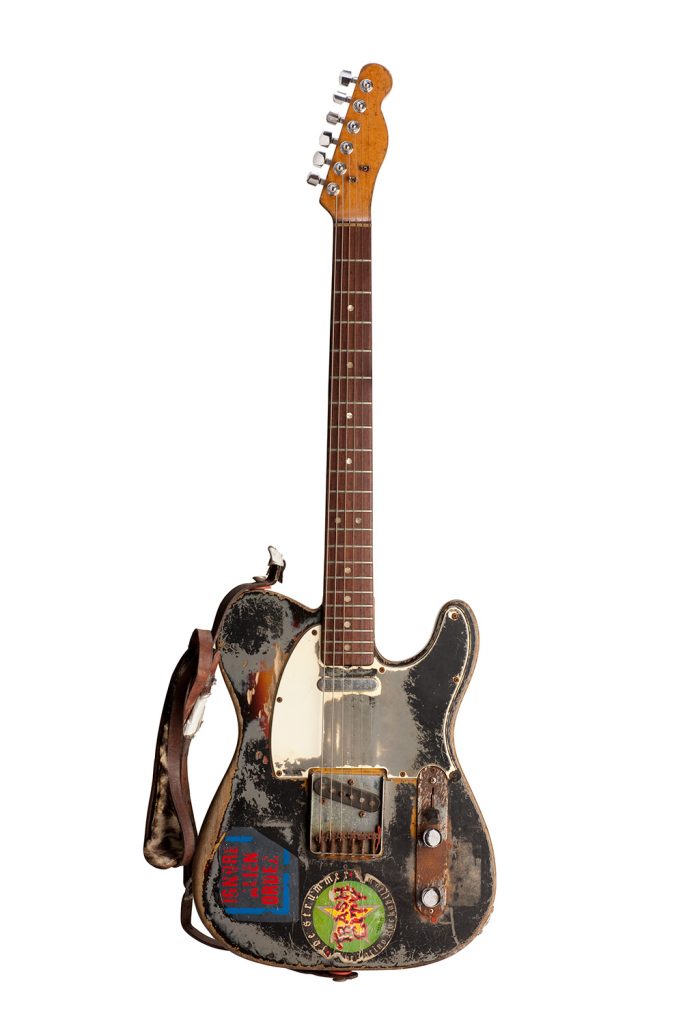 This guitar was Joe Strummer’s principal instrument. He played it in the studio while with the Clash and throughout his solo career. After he acquired the guitar in the early 1970s, Strummer took the guitar to an auto-body shop, where he had it spray painted with gray primer. 